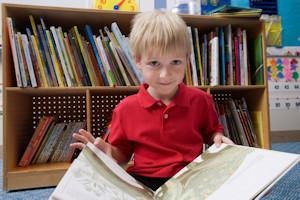 Six year old child sitting on the ground looking at an open book.