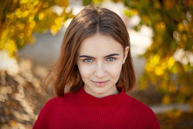 A girl with shoulder length hair tucked behind one ear and a red sweater looking directly at us.