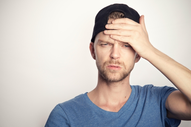 Man in his thirties with his hand on his forehead looking confused.