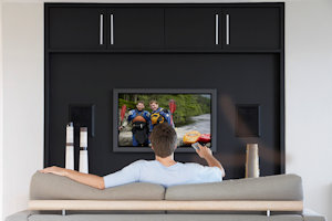 Back view of mid-adult man changing channels with television remote control in living room