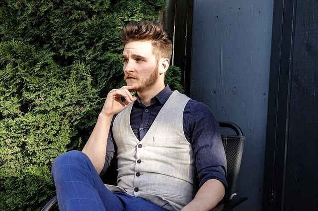 young man sitting in a chair wearing a vest with his hand on his chin