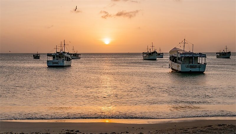 Boats at anchor as the sun sets over the sea.