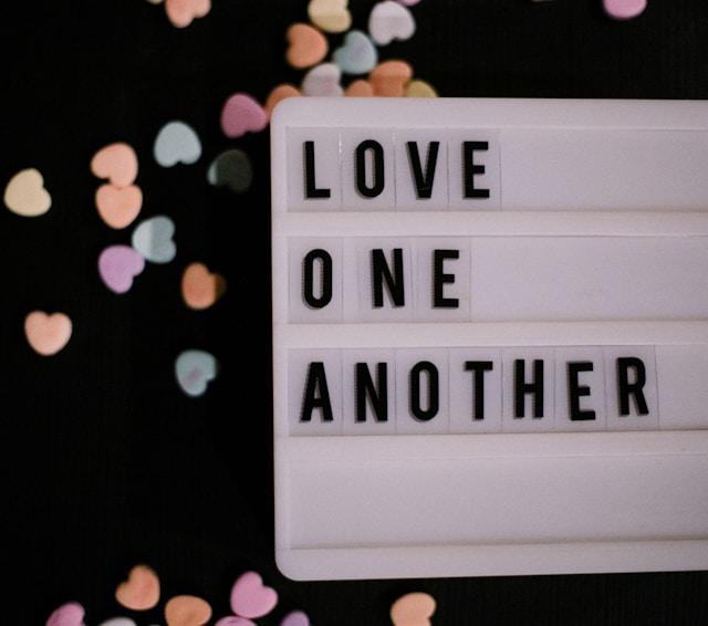A letter-slide sign that reads "Love One Another" on a black background with several small colored hearts.
