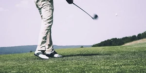 A photo of the green, the sky and the golfer from the waist down, mid swing.