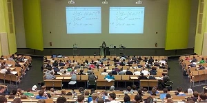 A college or university lecture room with auditorium seating as seen from the back looking toward the podium and lecturer.
