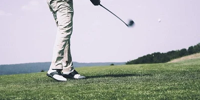 A photo of the green, the sky and the golfer from the waist down, mid swing.