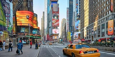 An image of a busy NYC street complete with people, billboards and yellow taxi.
